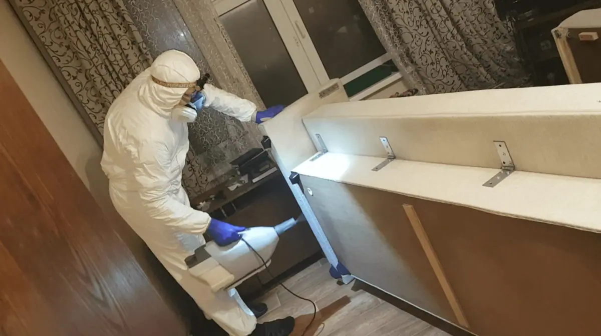 Фото: специалист по дезинсекции в защитном костюме обрабатывает диван от клопов. Профессиональная дезинфекция мягкой мебели в Липецке — НИМФАДЕЗ.
